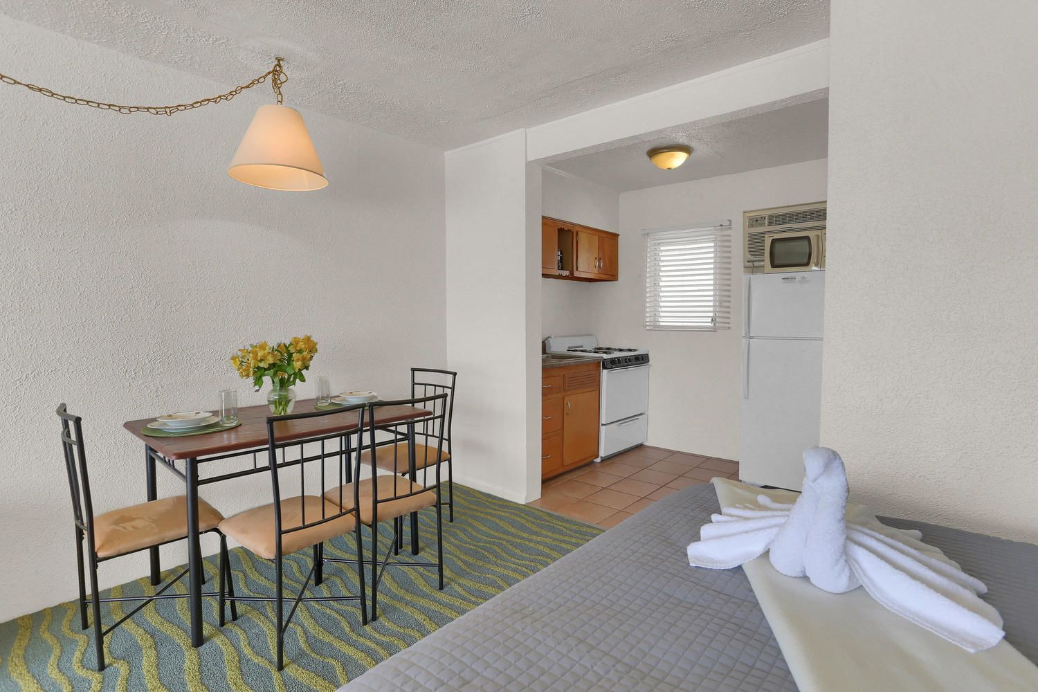 A compact kitchen with a stove, oven, and refrigerator. There is a dining area with a table and chairs, and a small seating area with a sofa and a towel.