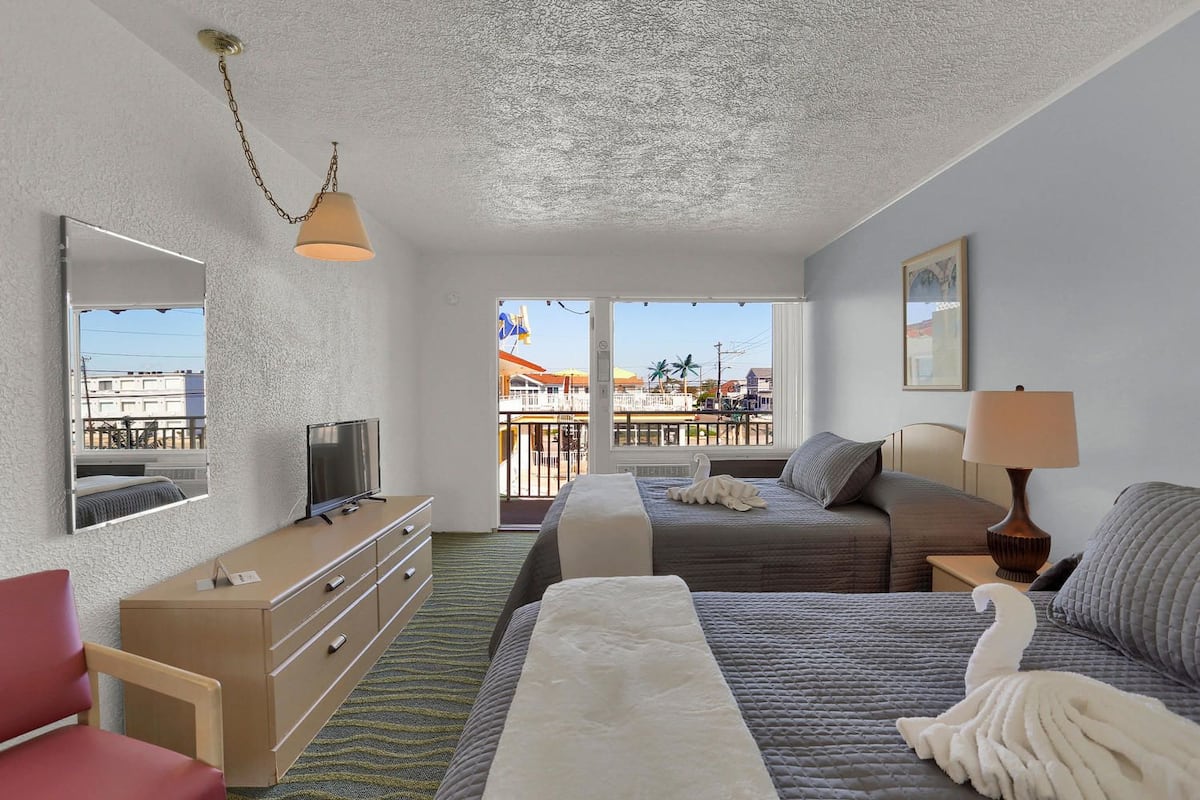 Habitación de hotel con cama, escritorio con televisor, cómoda, silla y balcón con vista a la ciudad.