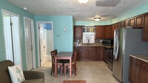 A living room with a sofa, a coffee table, and a dining area with chairs. The kitchen has wooden cabinets, a refrigerator, and a microwave. - Ala Kai Motel (Wildwood Crest)