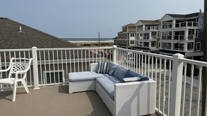 A balcony with a wicker sofa and a white chair, overlooking a beach and adjacent buildings. - Ala Kai Motel (Wildwood Crest)