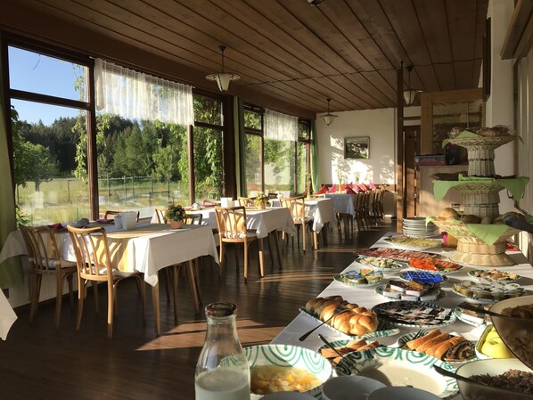 A dining area with tables set for breakfast, large windows, and a view of greenery outside.