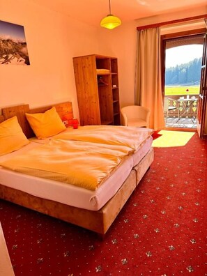 Une chambre d’hôtel avec un grand lit, une armoire en bois, une chaise et un balcon avec vue.