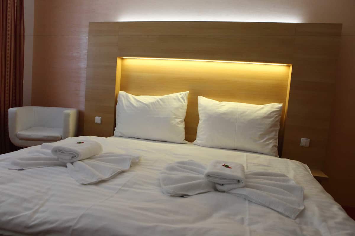 Een hotelkamer met een net opgemaakt bed, twee kussens, een stoel en handdoeken.