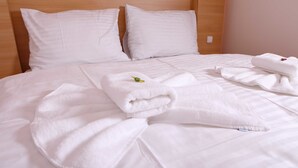 A neatly made bed with white linens and towels, a wooden headboard, and a small decorative item on one pillow.