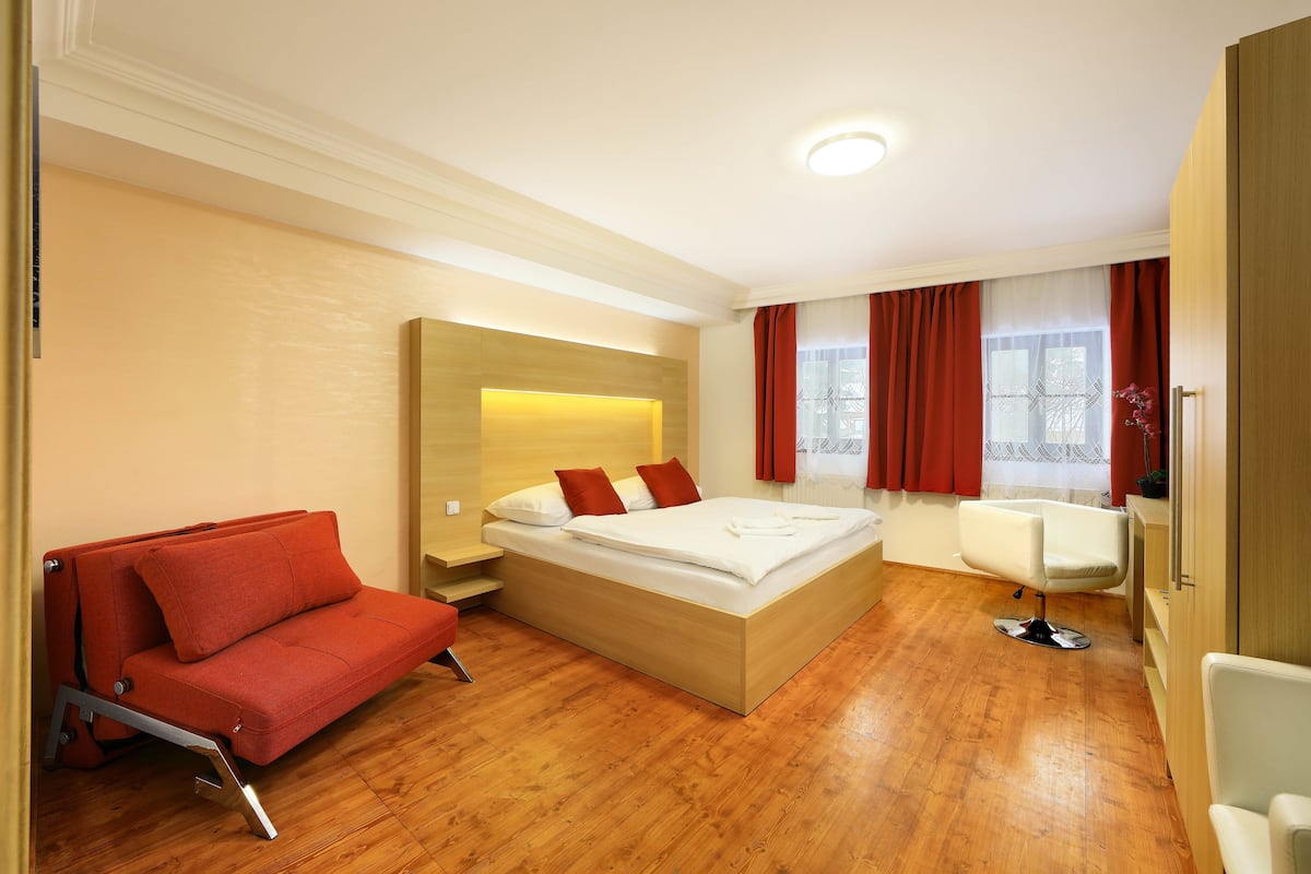 Een moderne hotelkamer met een houten vloer, een bed met rode kussens, een rode bank en een kappersstoel.