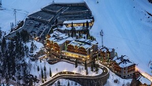 A snow-covered hotel with multiple buildings, a parking lot, and a ski slope in the background.