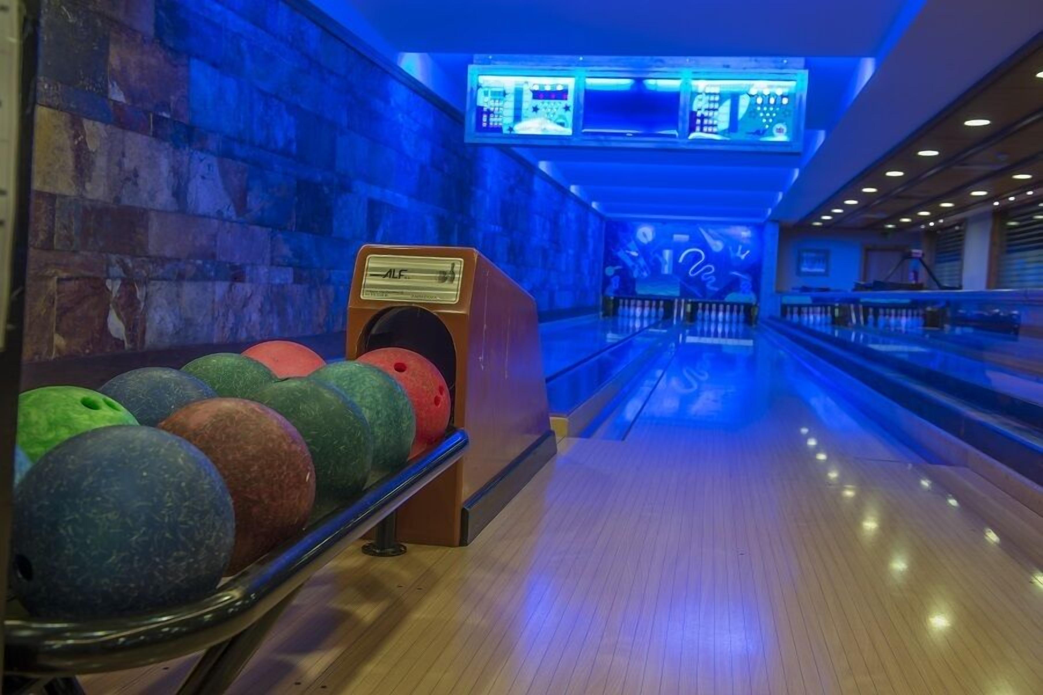 A bowling alley with multiple lanes, a bowling ball rack, and overhead scoreboards.