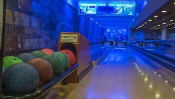 A bowling alley with multiple lanes, a bowling ball rack, and overhead scoreboards.