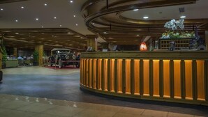 A lobby with a reception desk, wooden paneling, and a seating area with tables and chairs.