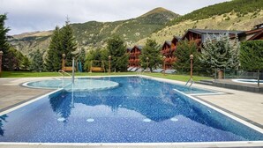A swimming pool with a mountain backdrop, surrounded by wooden cabins and trees.