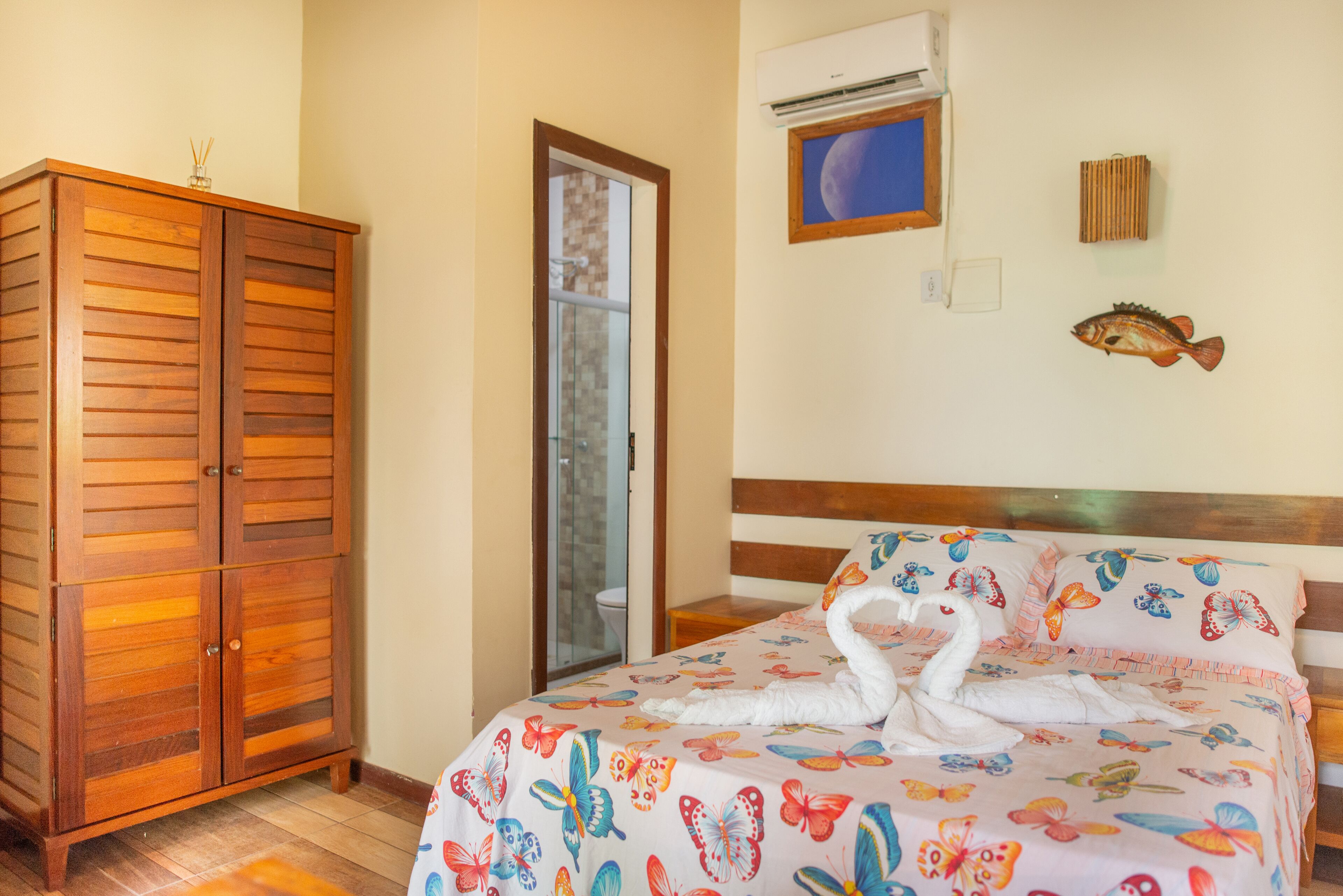 A bedroom with a wooden wardrobe, a bed with a butterfly-themed bedspread, and a wall-mounted air conditioner.