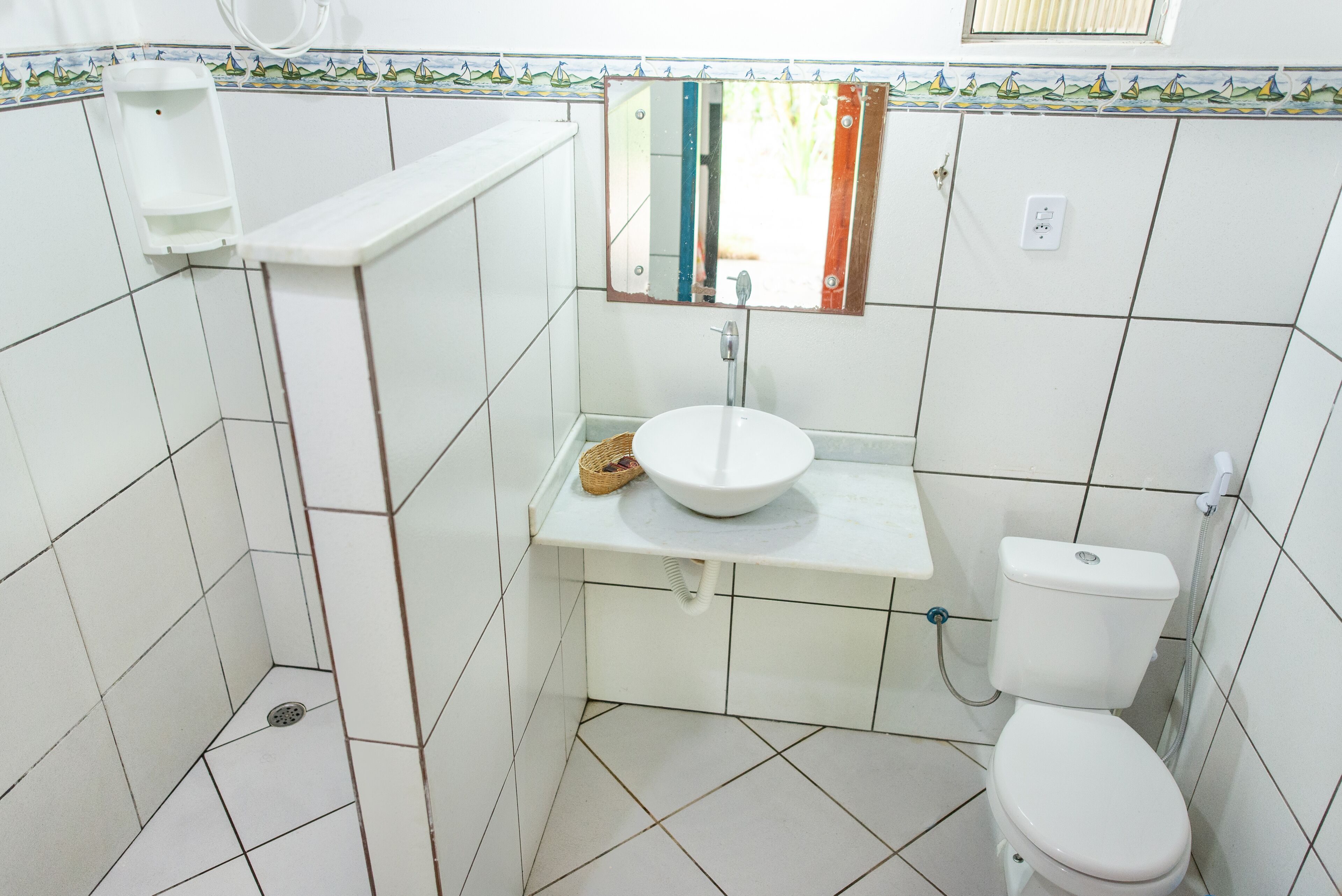 Un baño con azulejos blancos, un lavamanos blanco, un inodoro y un espejo.