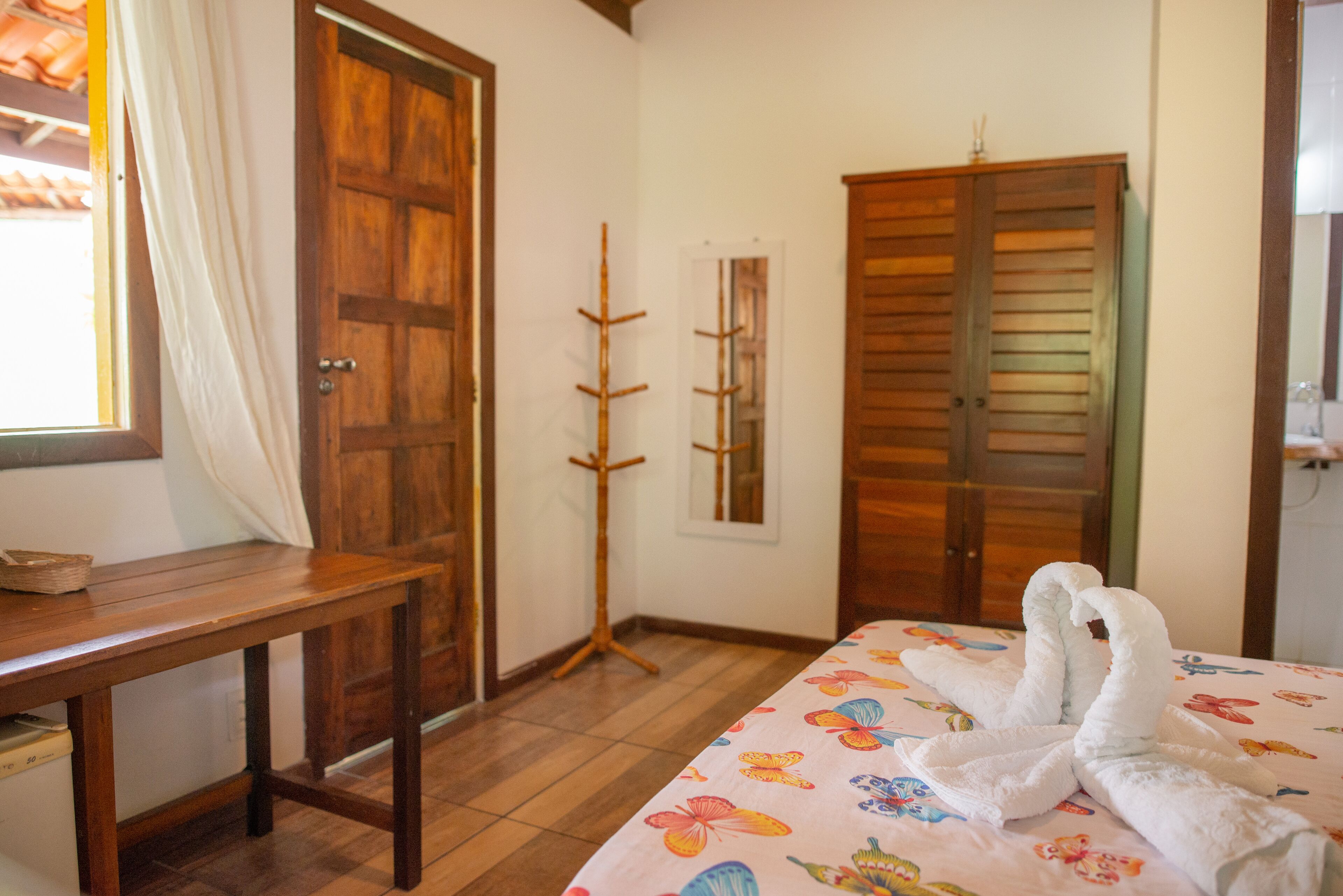 A room with a bed, a wooden table, a window with curtains, and a wooden wardrobe.