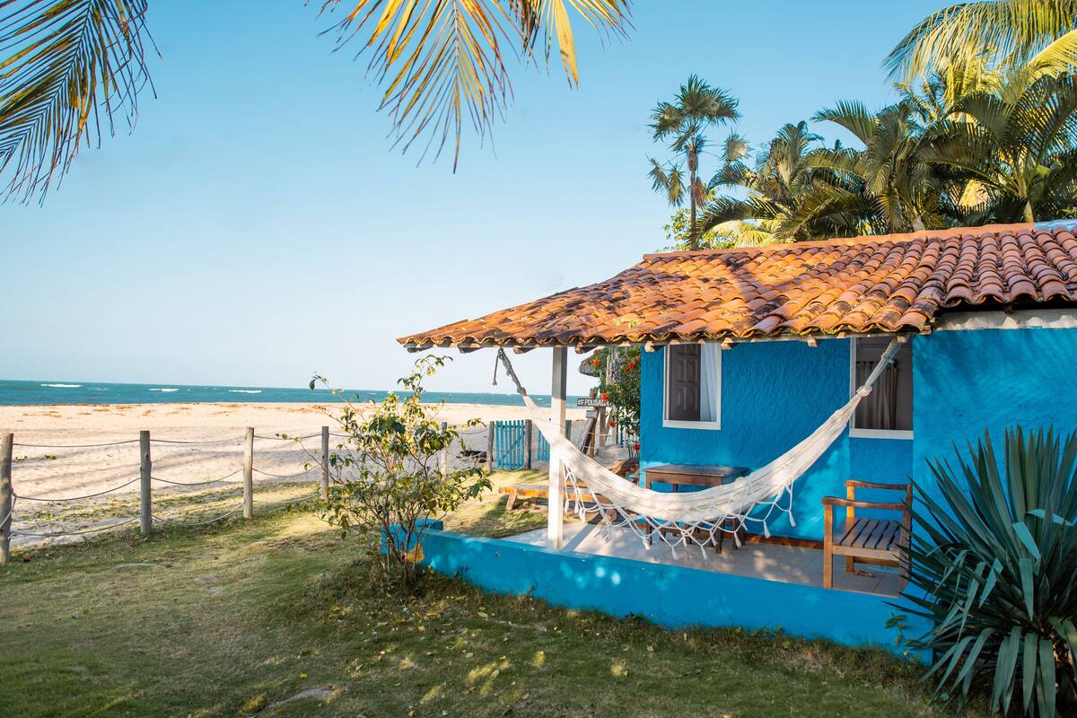 Uma casa de praia com rede, banco de madeira e vista para o oceano.