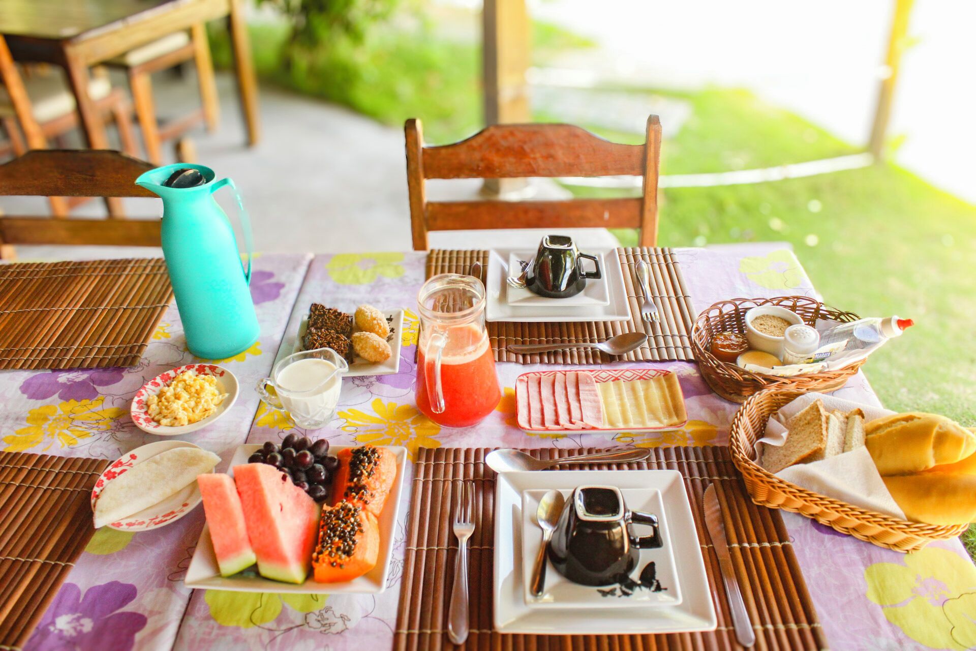 A table set with breakfast items including bread, eggs, and fruit, with a view of greenery in the background.