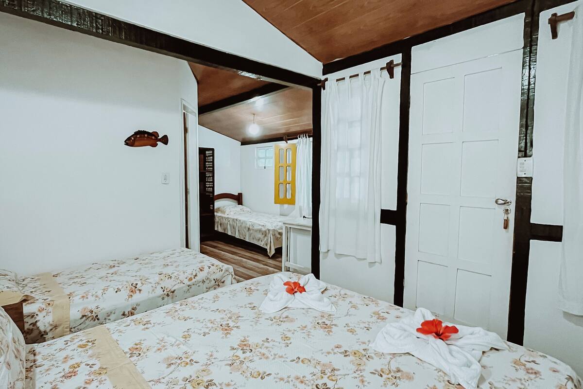 Quarto com duas camas de solteiro, teto de madeira, paredes brancas e porta com moldura preta.