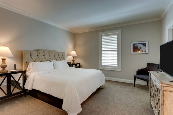 A neatly arranged bedroom with a large bed, two bedside tables with lamps, a chair, and a TV on a wooden cabinet.