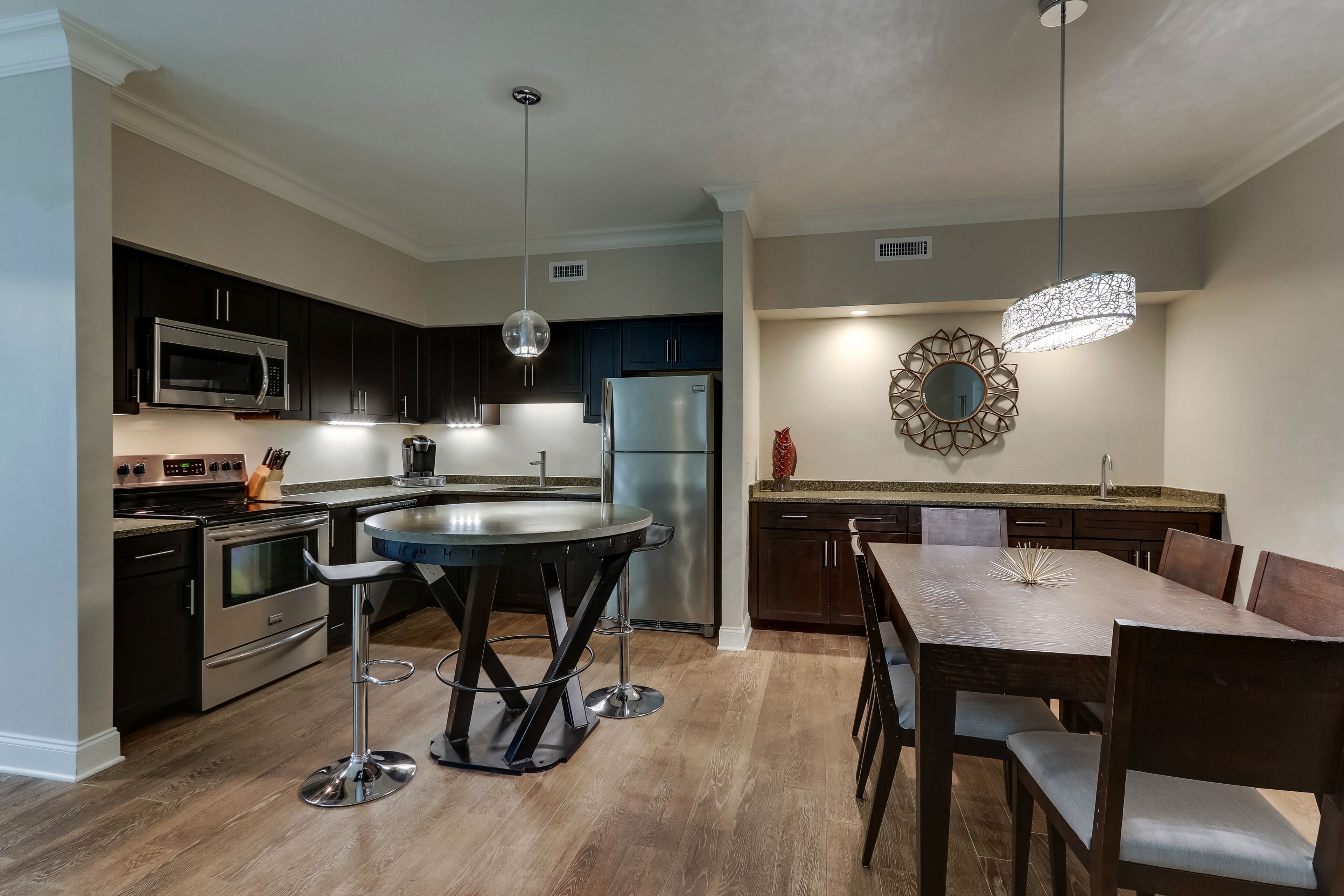A modern kitchen with dark cabinets, stainless steel appliances, a round dining table, and a pendant light.