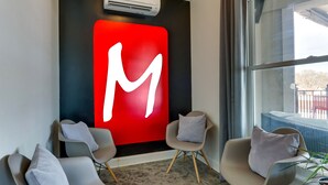Un interno moderno con un grande cartello rosso con la lettera 'M', due poltrone grigie e un'ampia finestra che si affaccia all'esterno.