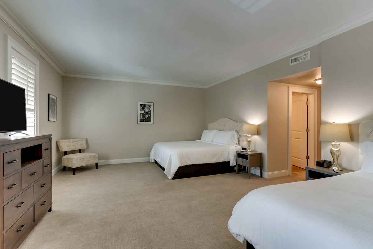 A hotel room with two beds, a dresser, a chair, and a television.