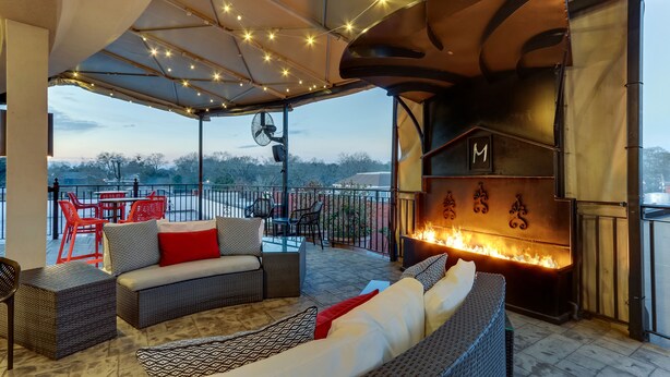 Patio esterno con mobili in vimini, un elemento decorativo con fuoco e luci a stringa.
