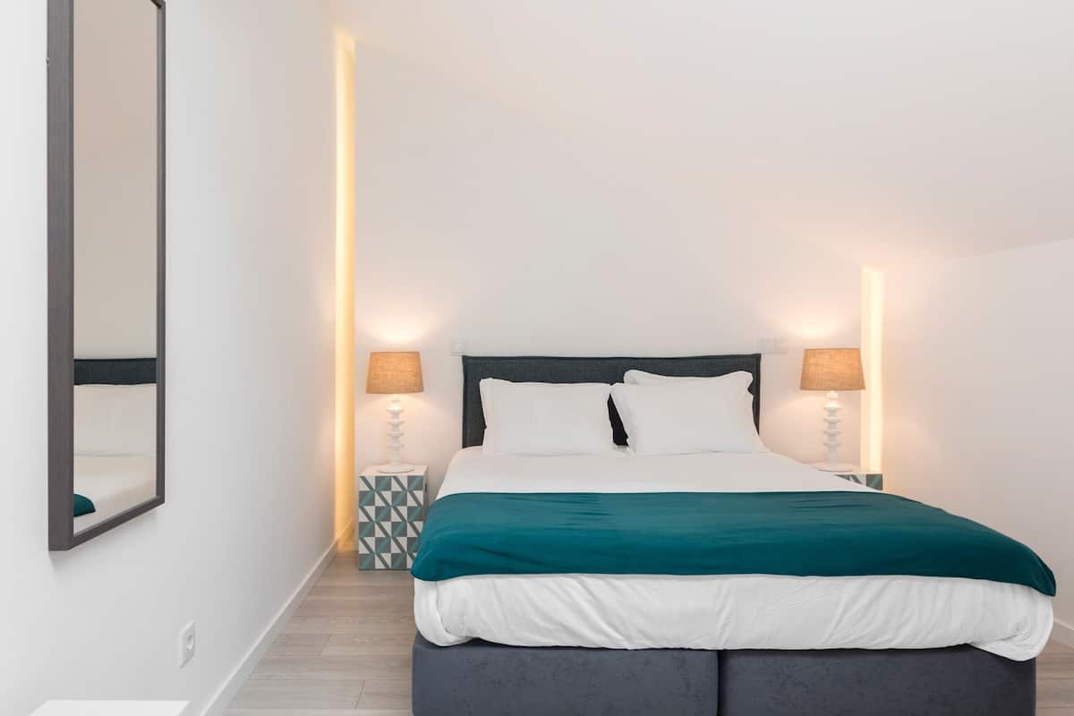 A modern bedroom with a bed, two bedside lamps, a nightstand, and a mirror.