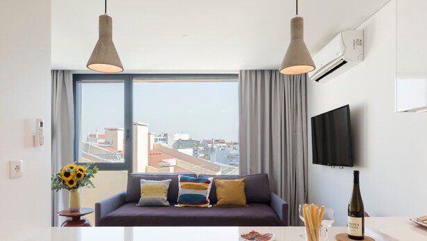Una sala de estar moderna con un sofá, un televisor y un comedor con una botella de vino.