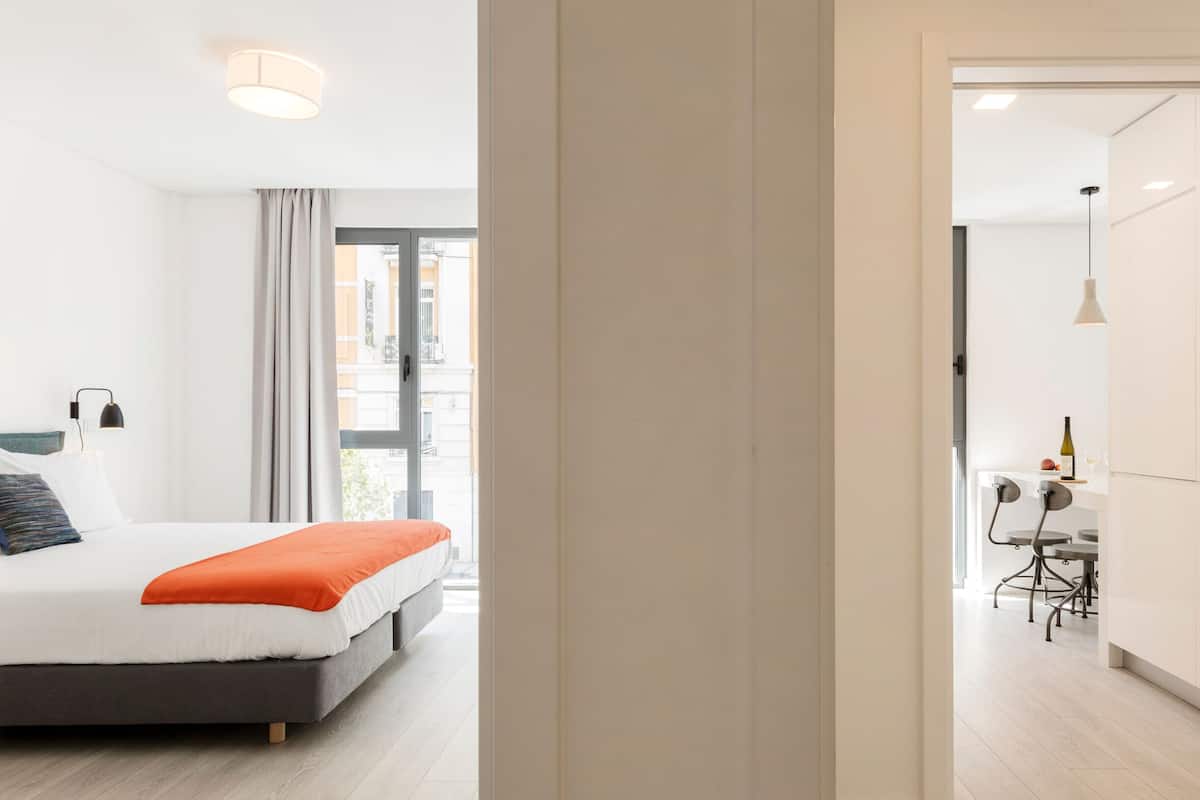 A modern hotel room with a bed, a desk, and a view of the city.