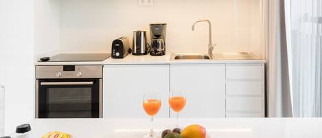 Une cuisine moderne équipée d’un four à micro-ondes, d’un grille-pain, d’une machine à café et d’un évier. On peut voir deux verres de jus d’orange et un saladier de fruits sur le comptoir.
