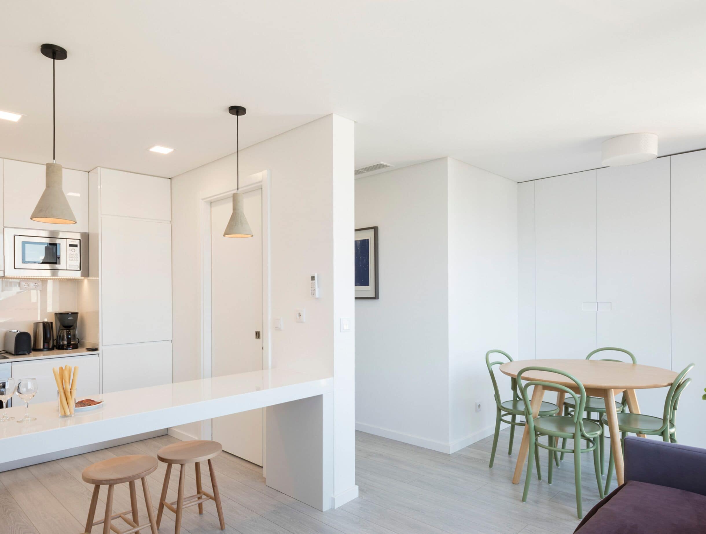 A modern kitchen with a white countertop, two bar stools, and pendant lighting.