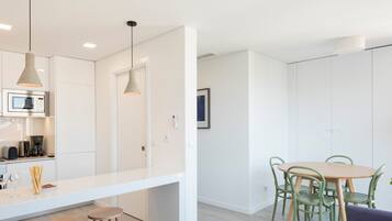 A modern kitchen with a white countertop, two bar stools, and pendant lighting.