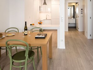 A modern kitchen with white cabinets, a wooden dining table, and green chairs.