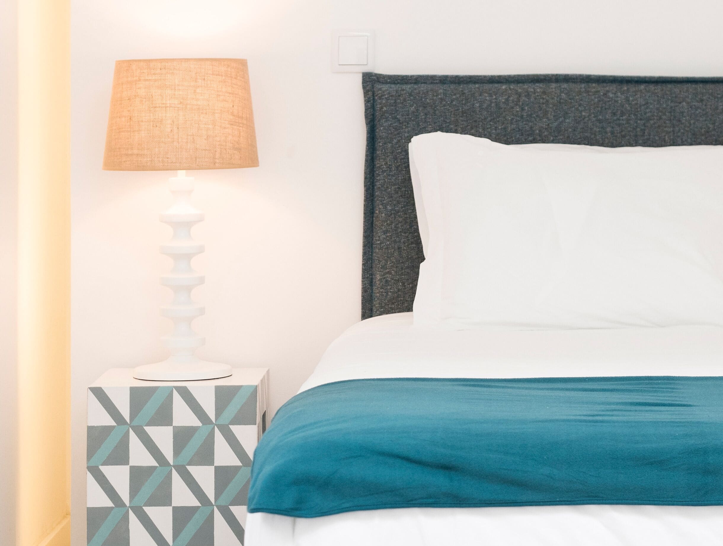 A neatly made bed with a teal blanket, a white pillow, and a grey headboard.