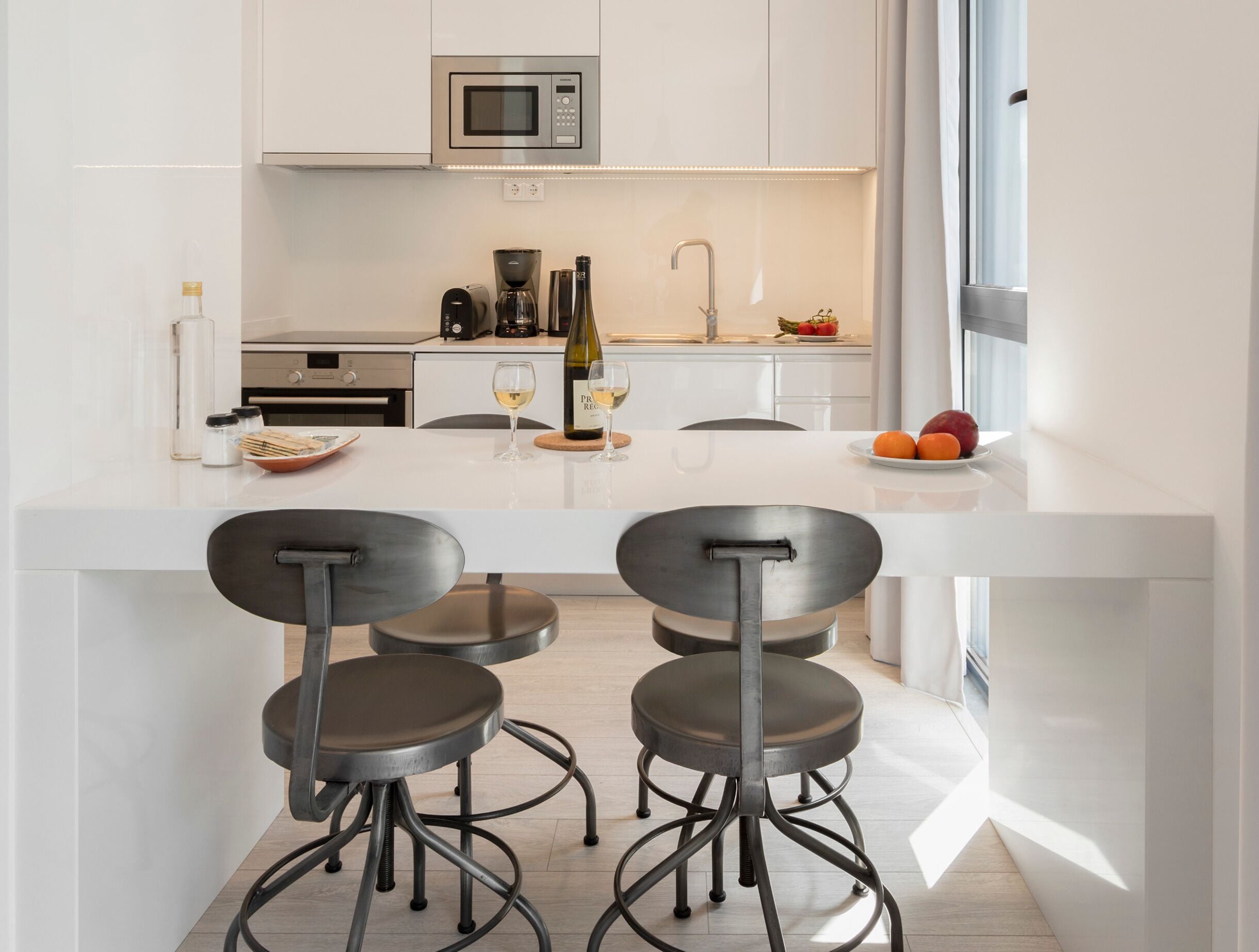A modern kitchen with a central island, bar stools, and a microwave.