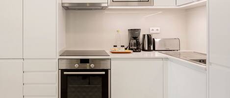 A modern kitchen with white cabinetry, a built-in microwave, a coffee maker, a toaster, and an oven.