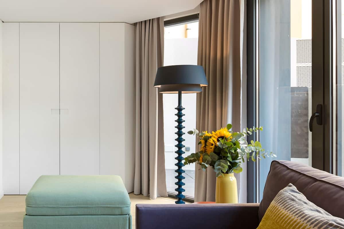 A modern living room with a sofa, ottoman, floor lamp, and a vase with flowers.