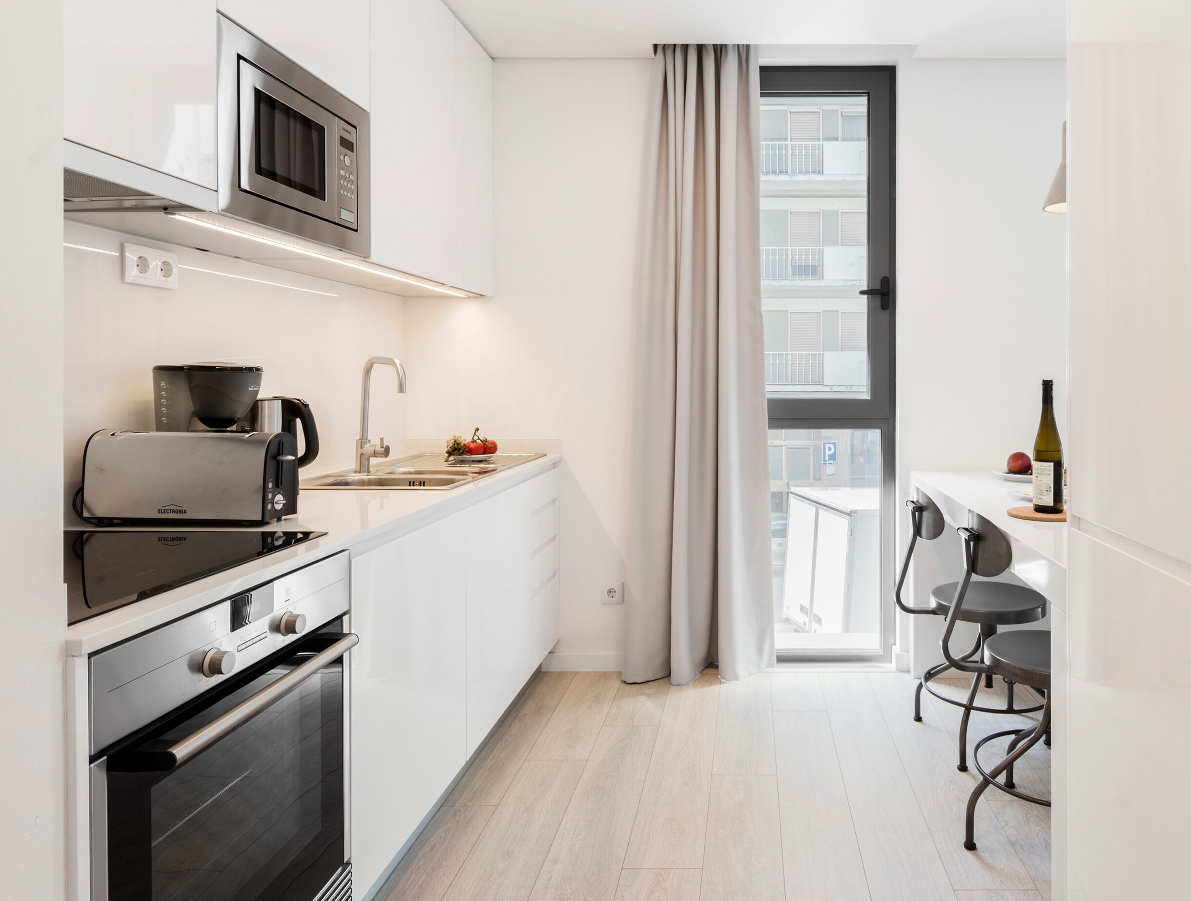Una cocina moderna con microondas, tostadora y estufa, un lavamanos con grifo, y un comedor con sillas y una mesa.