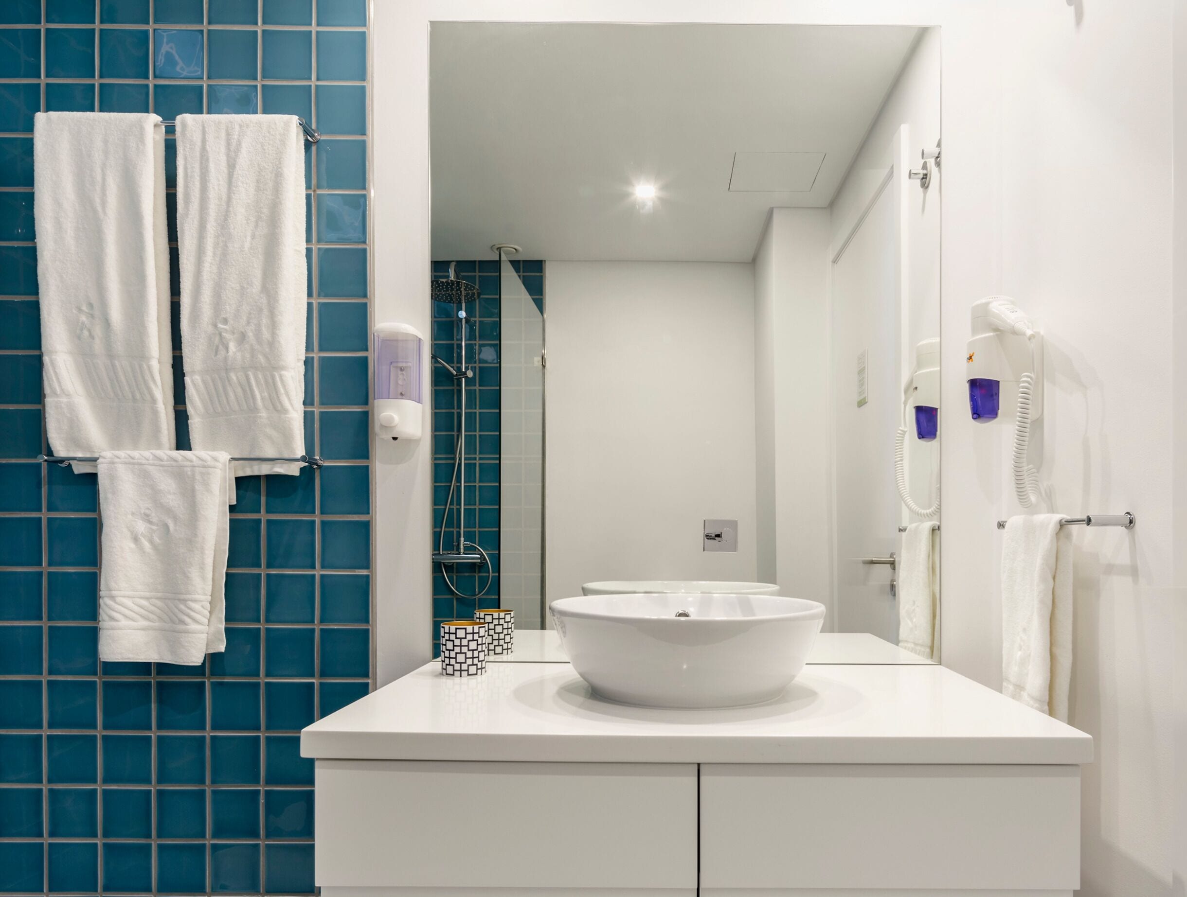 A modern bathroom with a white sink, two white towels, a handheld showerhead, and a white toilet.