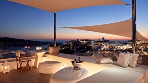 A rooftop terrace with a white sofa, a dining table, and a champagne bucket.