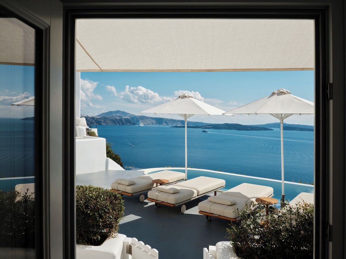 A balcony with white lounge chairs and umbrellas overlooking a body of water with mountains in the background.