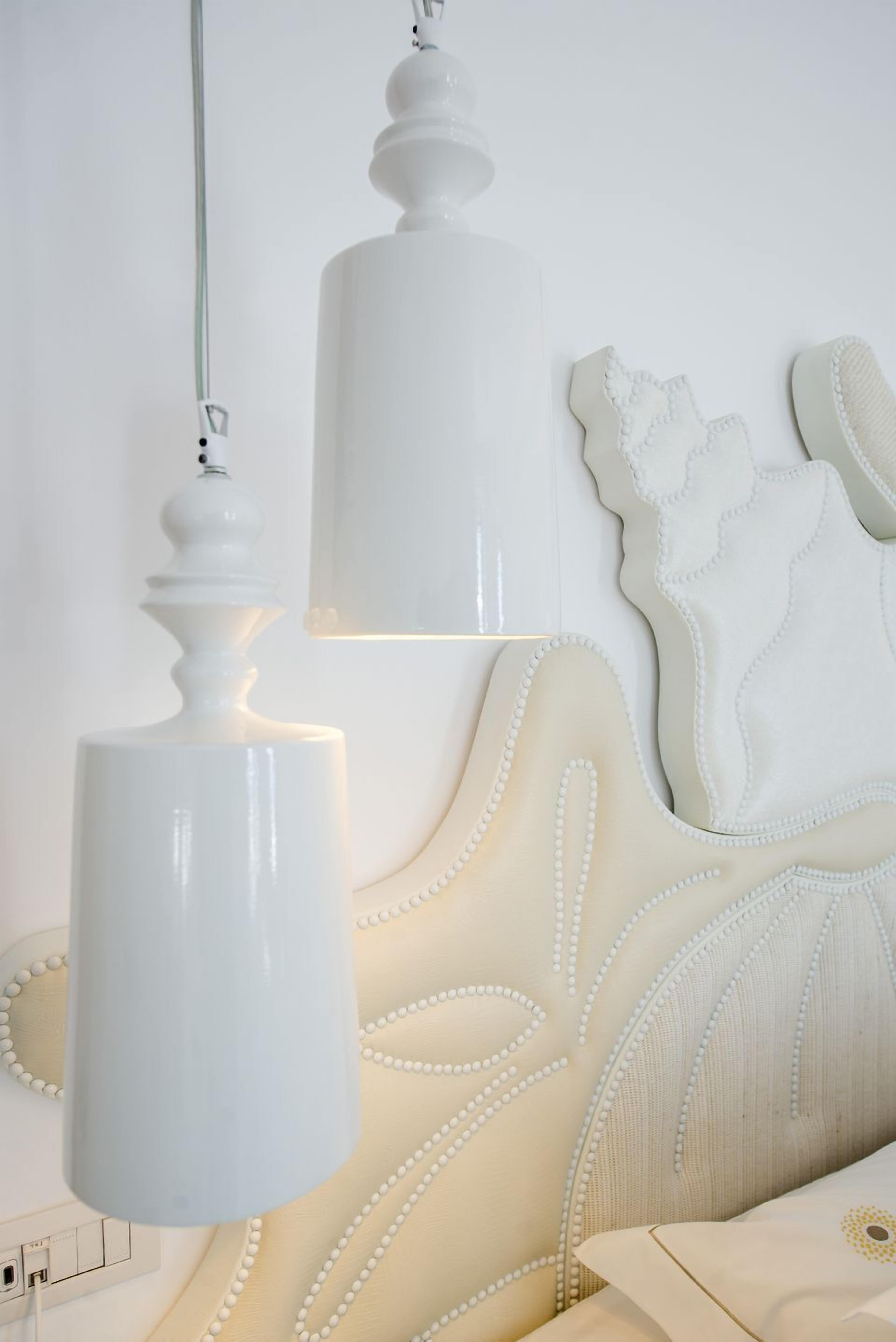 A bed with a white headboard and a white lamp hanging above it.