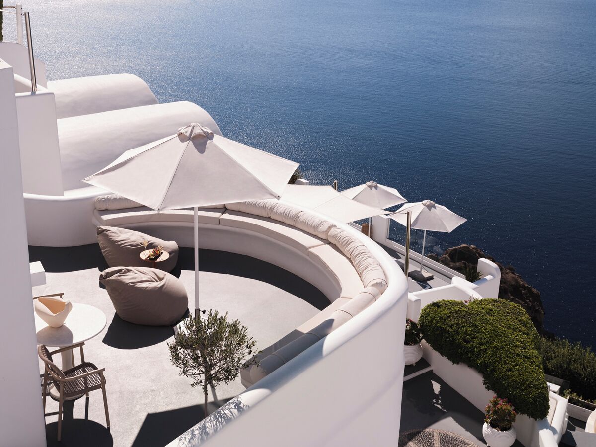 A modern outdoor seating area with a curved bench, a small table, and a potted plant, overlooking a body of water.