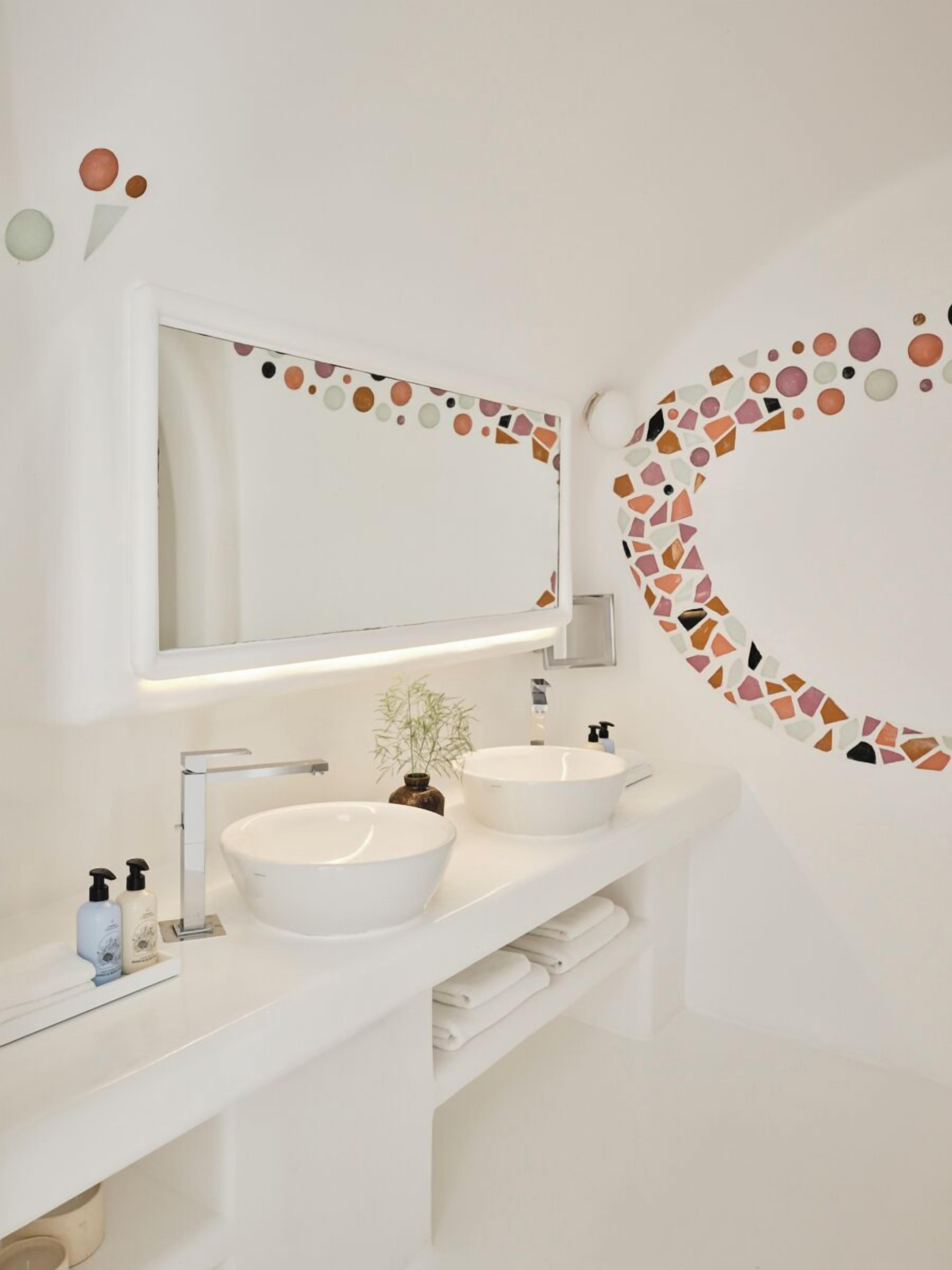 A modern bathroom with two white sinks, a large mirror, and a mosaic wall design.