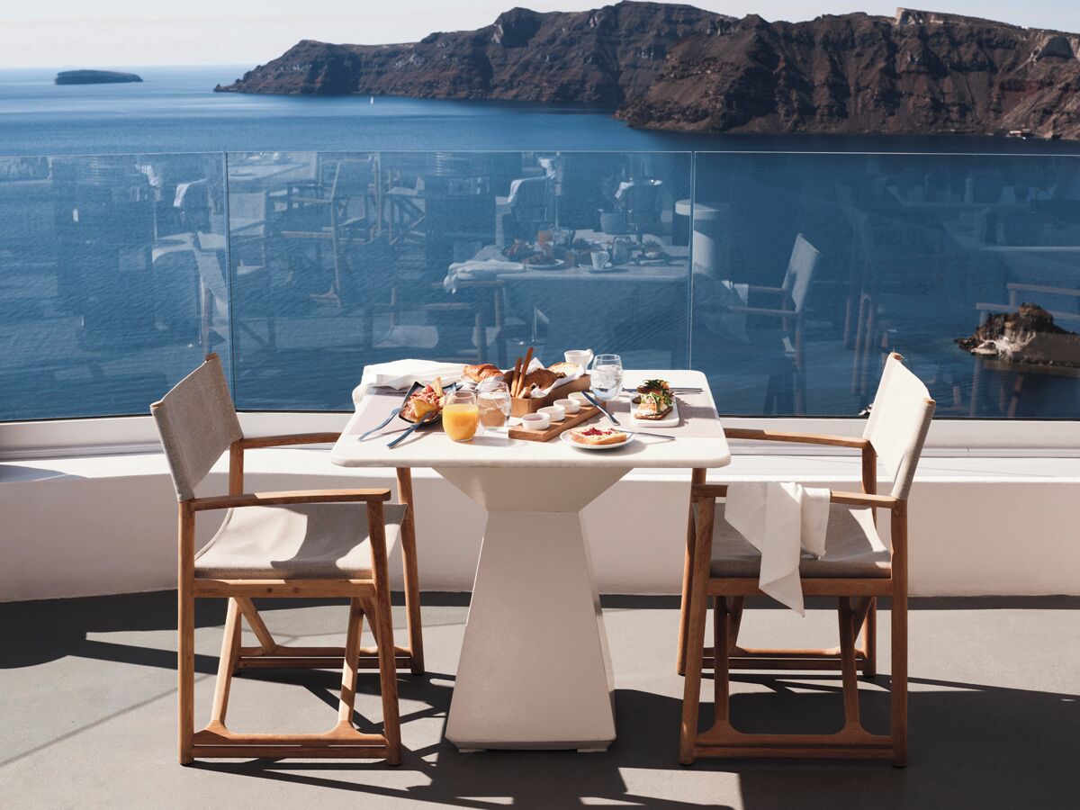 Une table à manger avec des chaises, offrant une vue sur la mer et une côte rocheuse.
