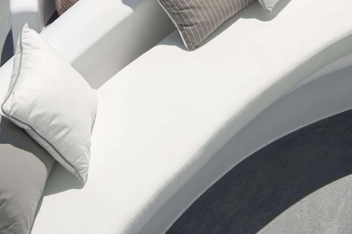 A poolside lounge area with white cushioned seating, a small potted plant, and a white umbrella.