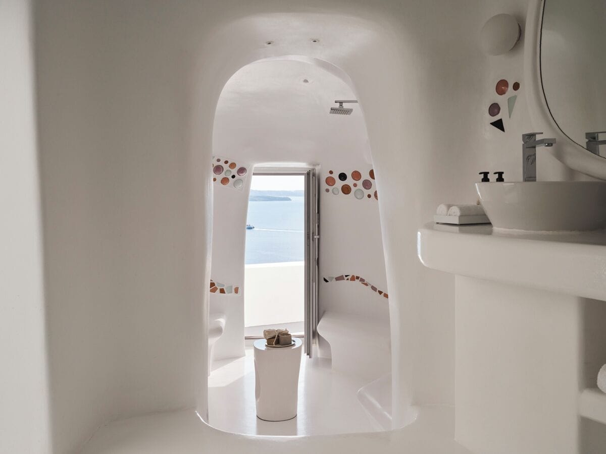 A modern bathroom with a white sink, a mirror, and a view of the sea through an arched doorway.