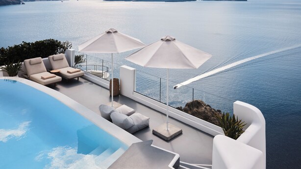 A modern infinity pool with a view of the sea, lounge chairs, and umbrellas.