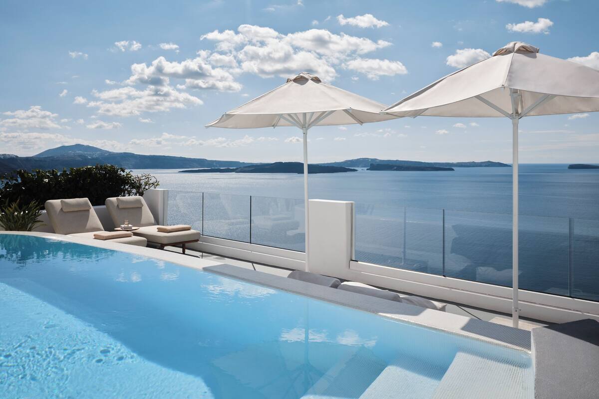 A poolside area with lounge chairs and umbrellas, overlooking a large body of water and distant land.