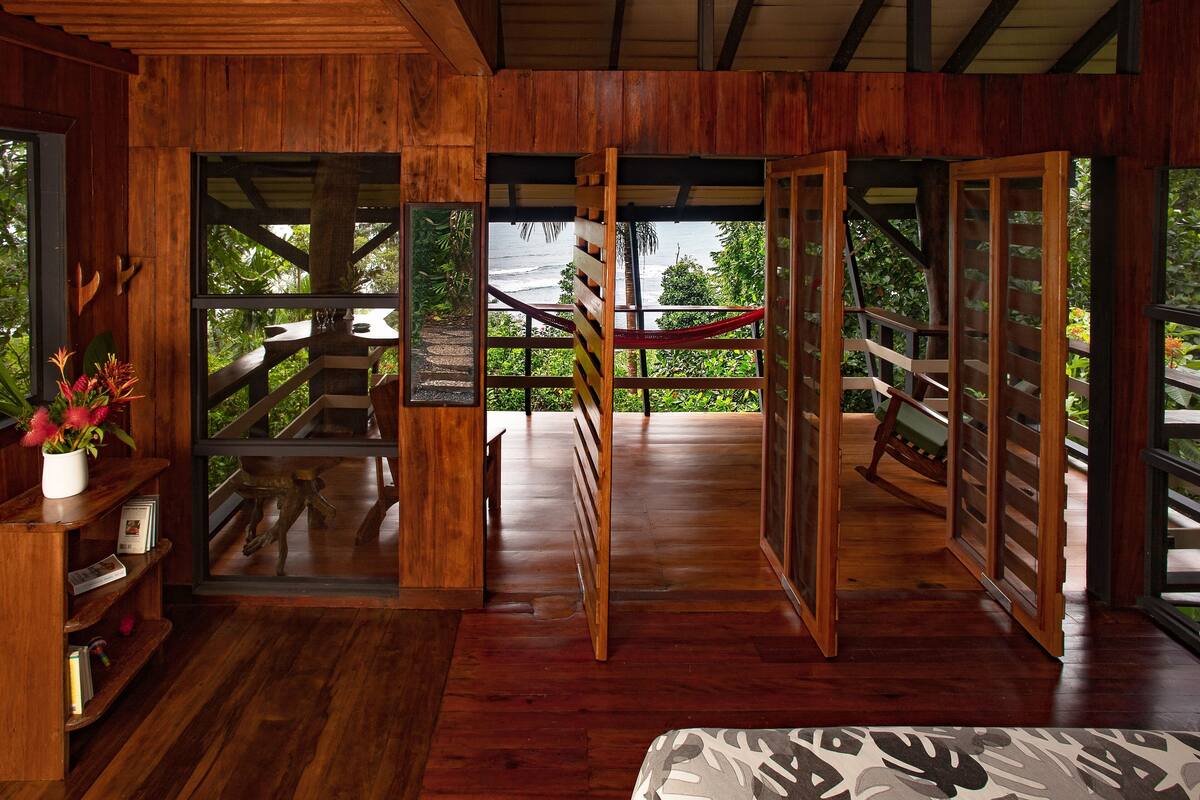 A wooden interior with a view of a wooden deck and a hammock.