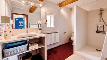 Une salle de bain avec un lavabo blanc, un miroir et une douche. Il y a une fenêtre au-dessus du lavabo et un radiateur en dessous.